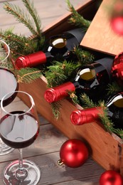 Wooden crate with bottles of wine, glasses, fir twigs and red Christmas balls on table