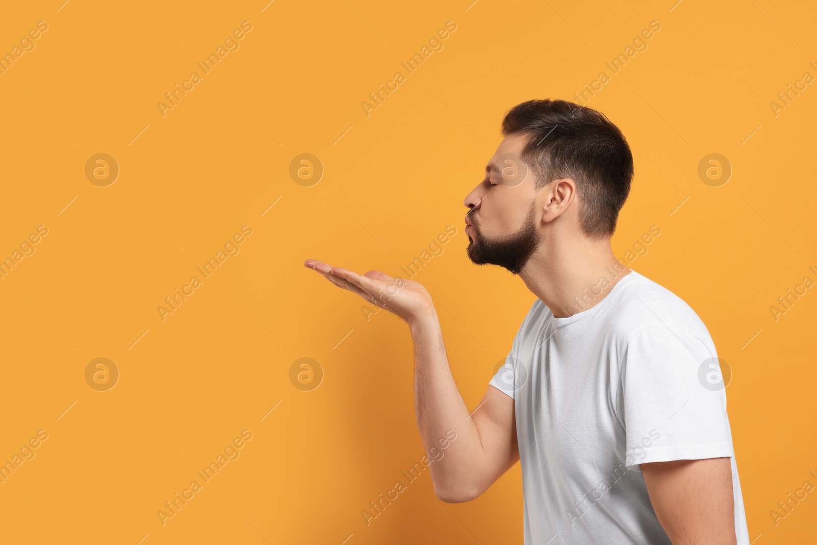 Photo of Handsome man blowing kiss on orange background. Space for text