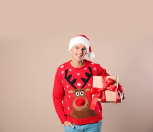 Happy man in Christmas sweater and Santa hat holding gift box on beige background