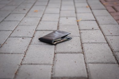 Black wallet on pavement outdoors. Lost and found