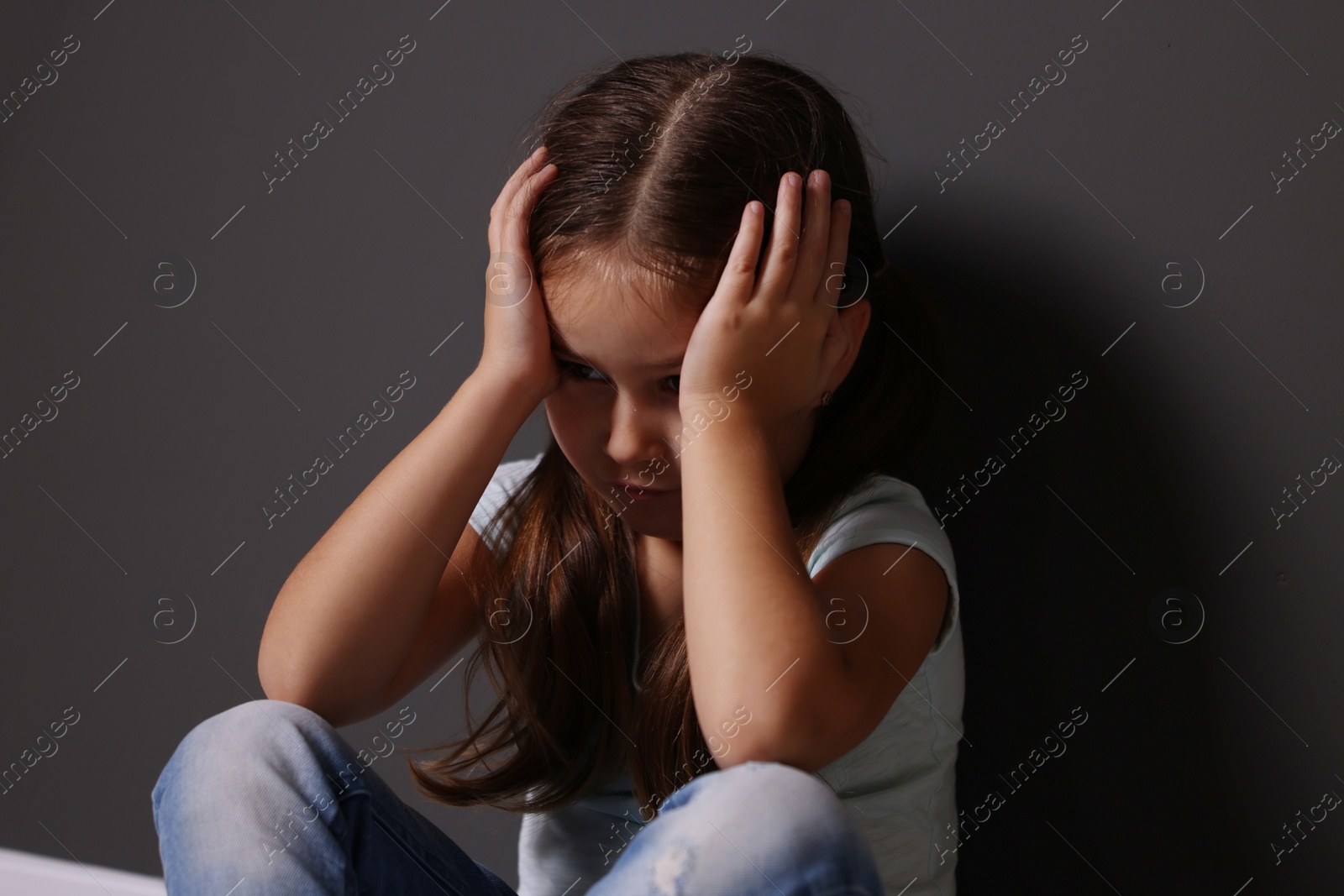 Photo of Child abuse. Upset little girl near gray wall