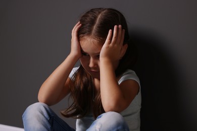 Photo of Child abuse. Upset little girl near gray wall