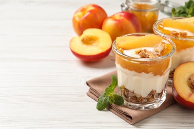 Photo of Tasty peach yogurt with granola, pieces of fruit and jam on white wooden table, space for text