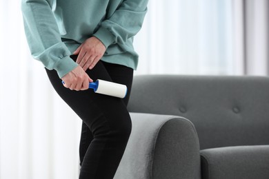 Photo of Woman with lint roller removing pet hair from black trousers indoors, closeup. Space for text