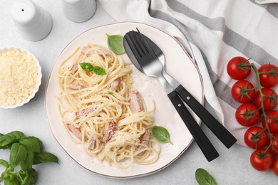 Plate of tasty pasta Carbonara with basil leaves on light grey table, flat lay