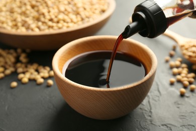 Photo of Pouring tasty soy sauce from bottle into bowl on black table, closeup