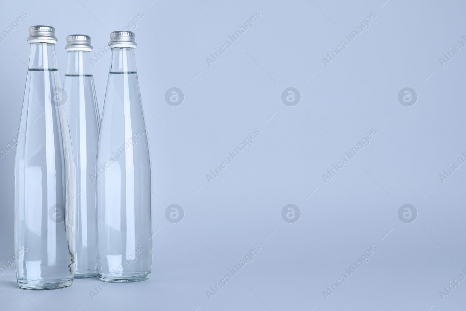 Photo of Glass bottles with water on white background, space for text