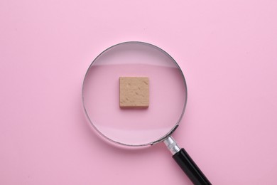 Photo of Looking at wooden cube through magnifying glass on pink background, top view