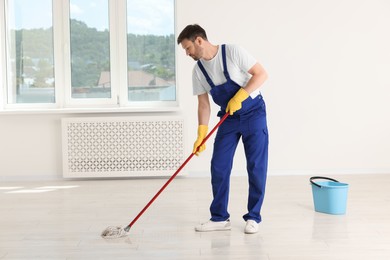 Photo of Man in uniform cleaning floor with mop indoors