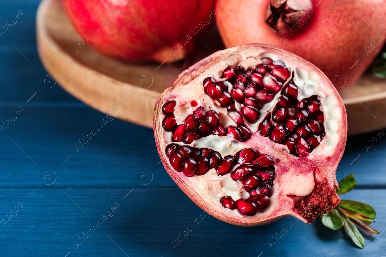 Photo of Delicious ripe pomegranates on blue wooden table, closeup