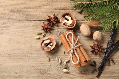 Different spices, nuts and fir branches on wooden table, flat lay. Space for text