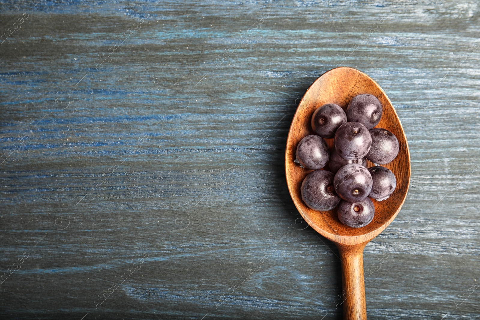 Photo of Spoon with fresh acai berries on wooden table, top view