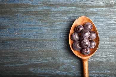 Photo of Spoon with fresh acai berries on wooden table, top view