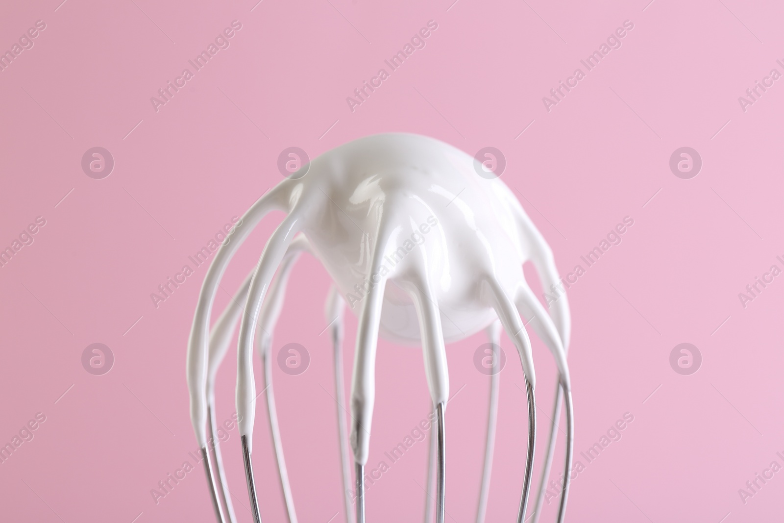 Photo of Whisk with whipped cream on pink background, closeup