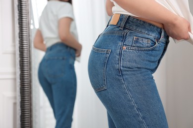 Photo of Woman in stylish jeans near mirror indoors, closeup. Space for text