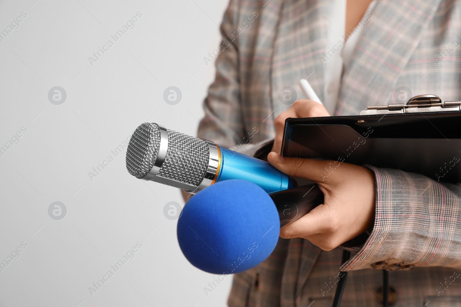 Photo of Journalist with microphones and clipboard on light background, closeup