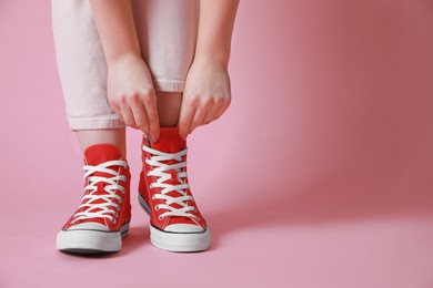 Photo of Woman wearing pair of new stylish sneakers on pink background, closeup. Space for text