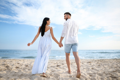 Photo of Happy young couple walking together on beach, back view