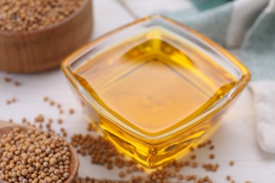 Photo of Bowl of natural oil and mustard seeds on white table, closeup