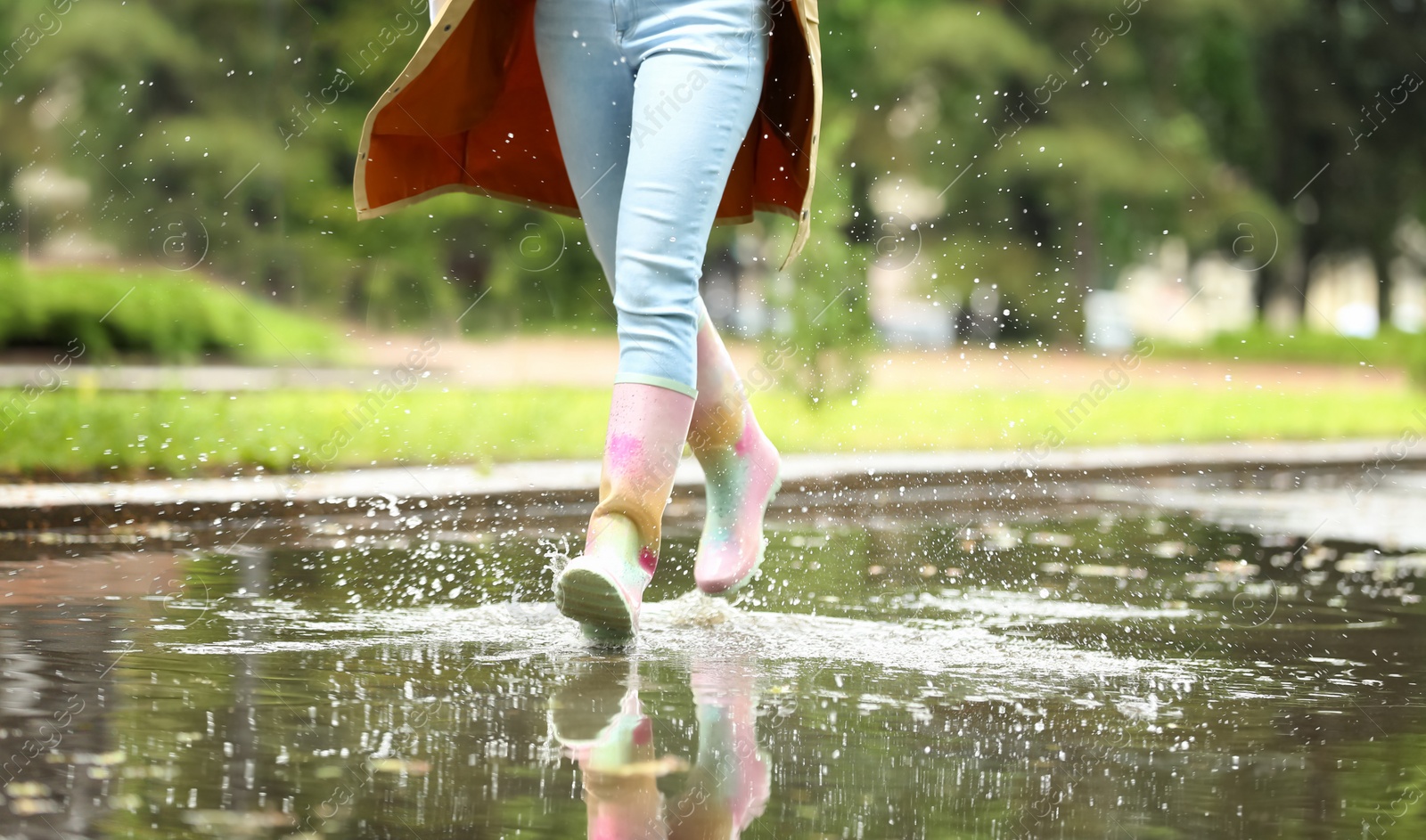 Photo of Woman with rubber boots running in puddle, closeup. Rainy weather