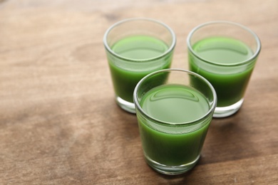 Photo of Glasses of wheat grass juice on wooden table. Space for text
