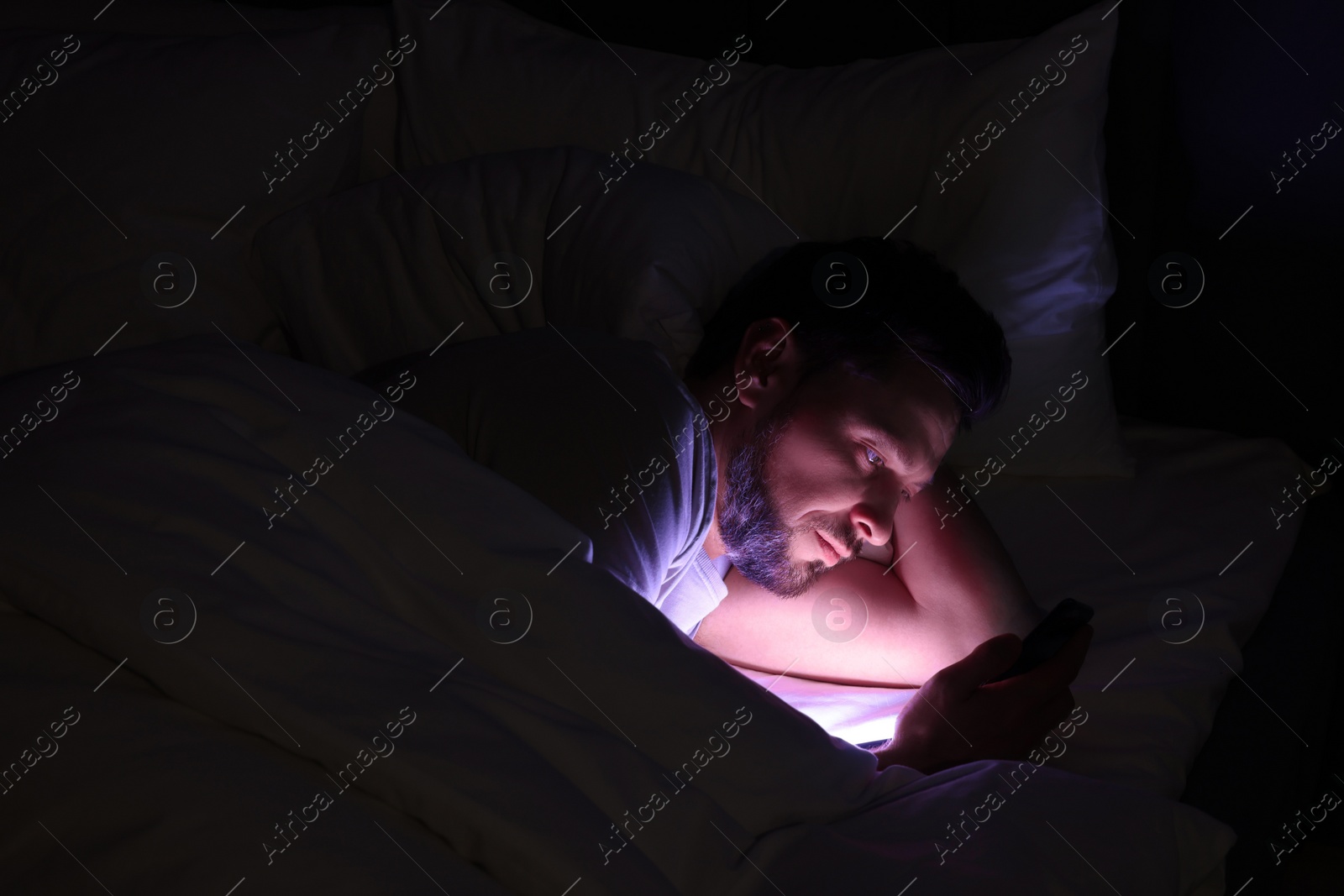 Photo of Man using smartphone in bed at night. Internet addiction