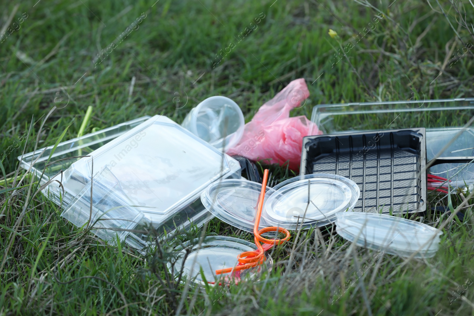 Photo of Used plastic tableware and bag on grass outdoors, closeup and space for text. Environmental pollution concept