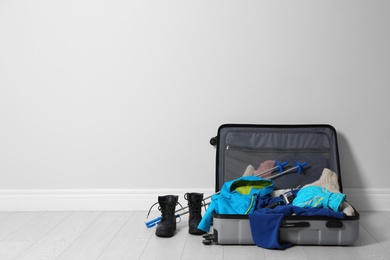 Photo of Open suitcase with warm clothes for winter vacation on wooden floor. Space for text