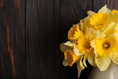 Photo of Bouquet of beautiful yellow daffodils in vase near wooden wall, closeup. Space for text