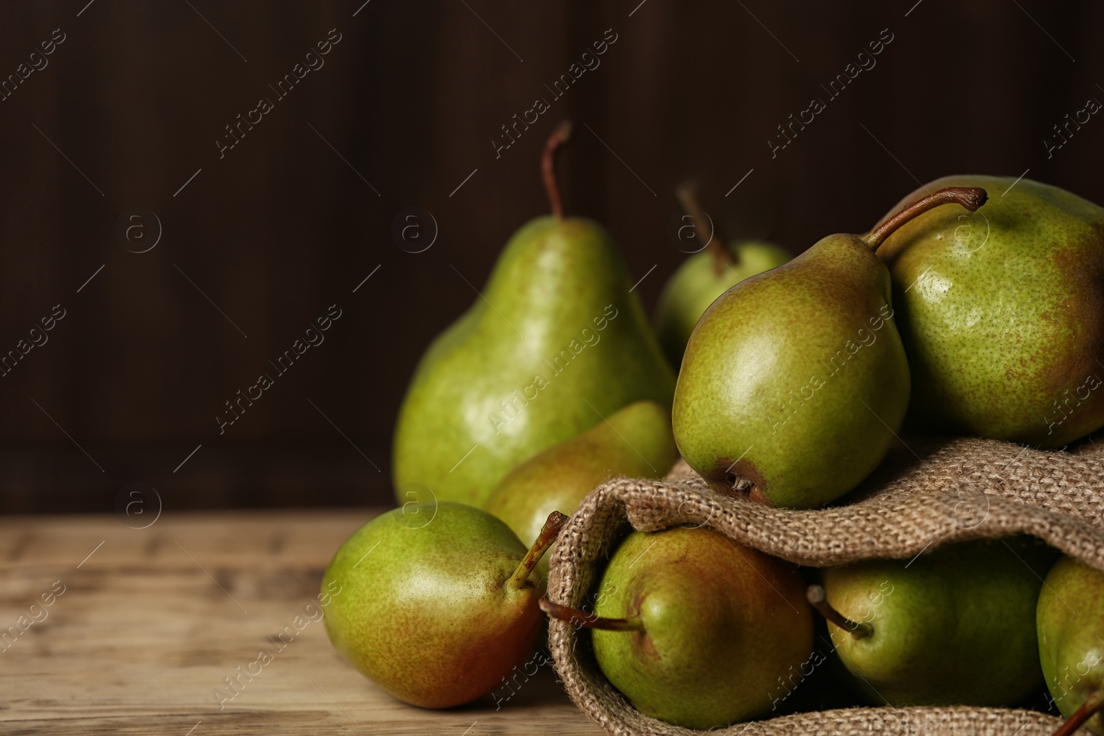 Photo of Fresh ripe pears on wooden table against dark background with space for text