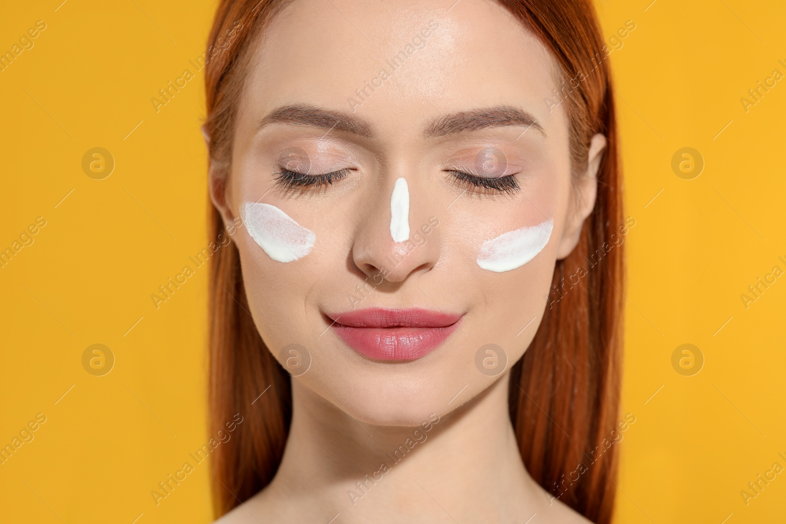 Photo of Beautiful young woman with sun protection cream on her face against orange background, closeup