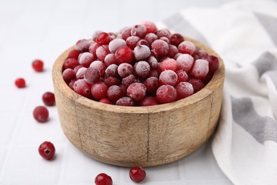 Photo of Frozen red cranberries in bowl on white tiled table, closeup