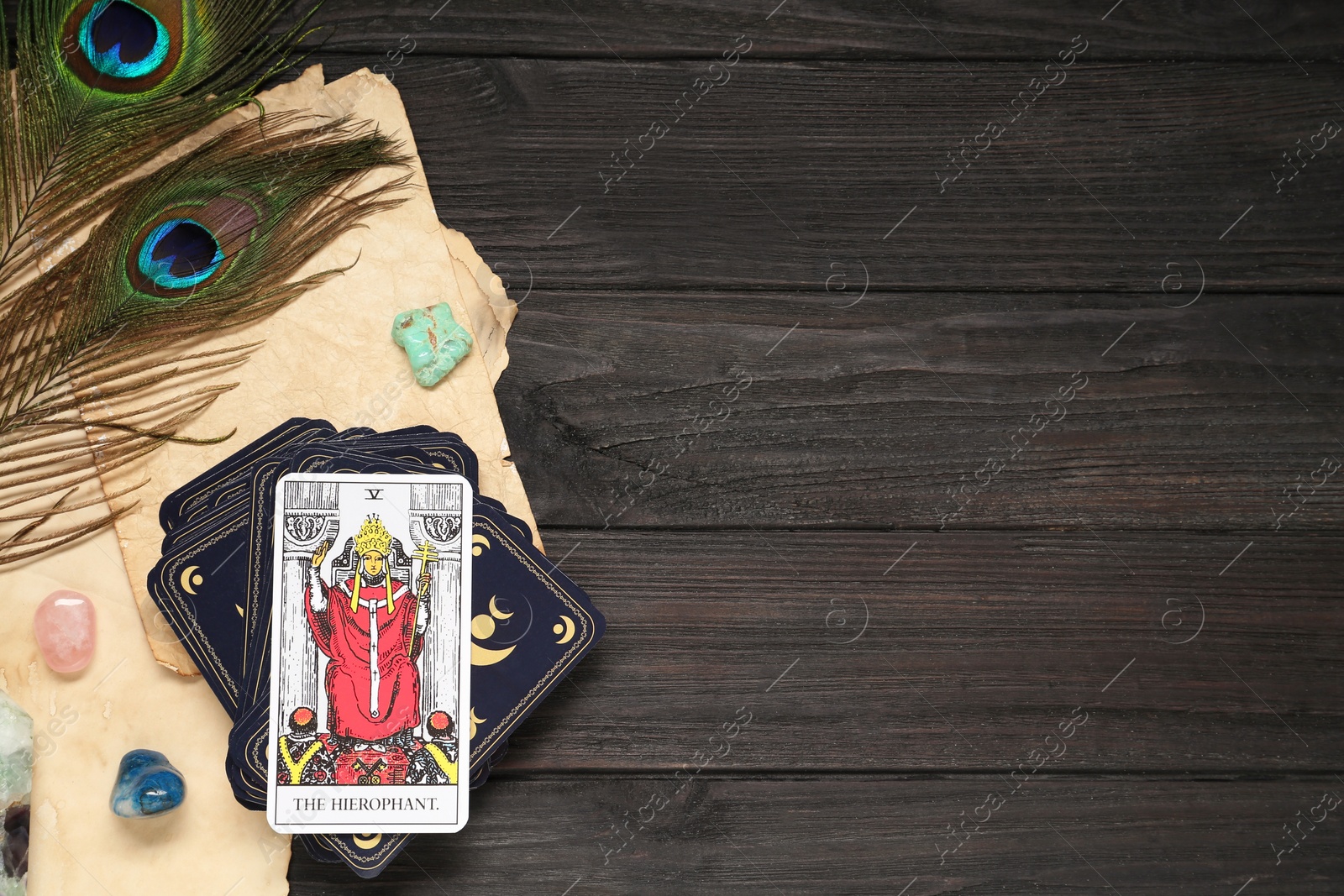 Photo of The Hierophant with other tarot cards near peacock feathers and gemstones on black wooden table, flat lay. Space for text