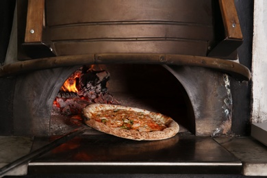 Photo of Oven with burning firewood and tasty pizza in restaurant kitchen