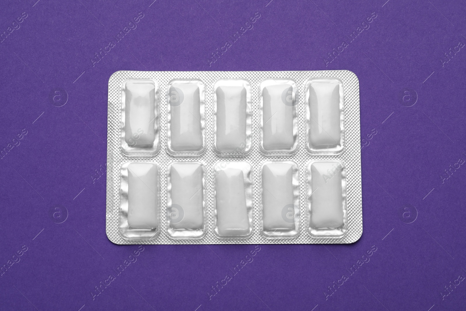 Photo of Blister of chewing gums on purple background, top view