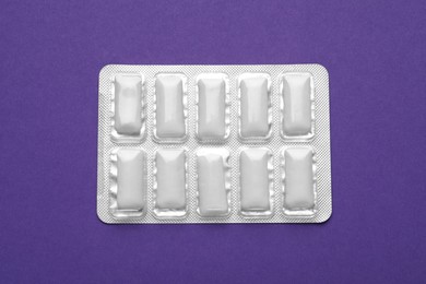 Photo of Blister of chewing gums on purple background, top view