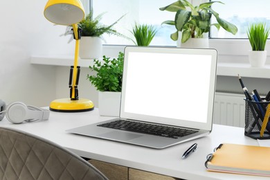 Image of Comfortable workplace at home. Modern laptop with blank screen and lamp on white desk. Mockup for design