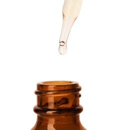 Photo of Essential oil dripping from pipette into glass bottle on white background