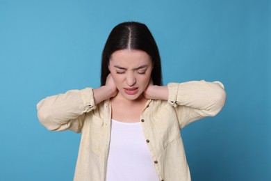 Photo of Young woman suffering from pain in neck on light blue background. Arthritis symptoms