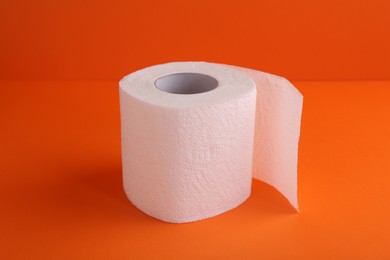 Photo of Soft toilet paper roll on orange background, closeup