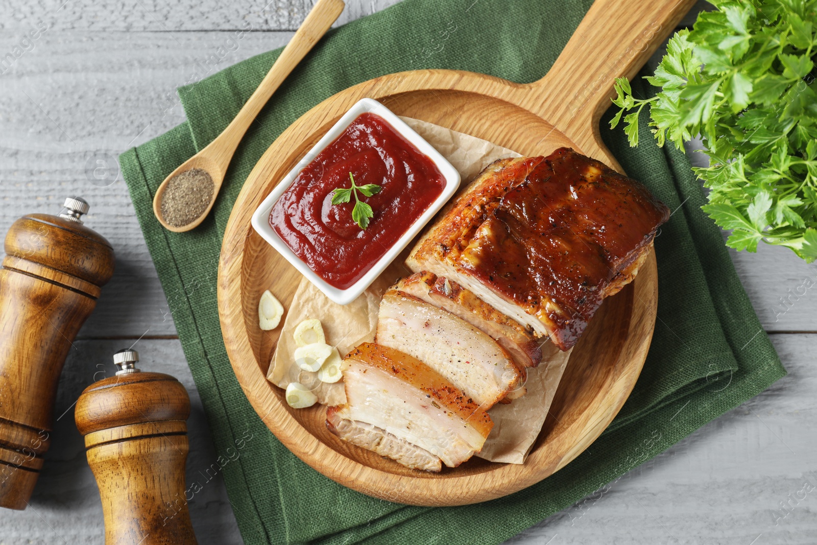 Photo of Pieces of baked pork belly served with sauce on grey wooden table, flat lay