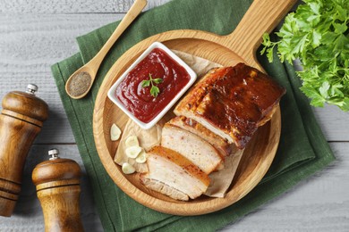 Photo of Pieces of baked pork belly served with sauce on grey wooden table, flat lay