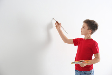 Little child painting on blank white wall indoors. Space for text