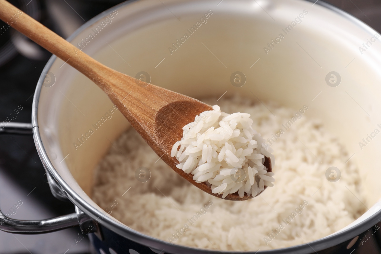 Photo of Wooden spoon with delicious rice over pot, closeup