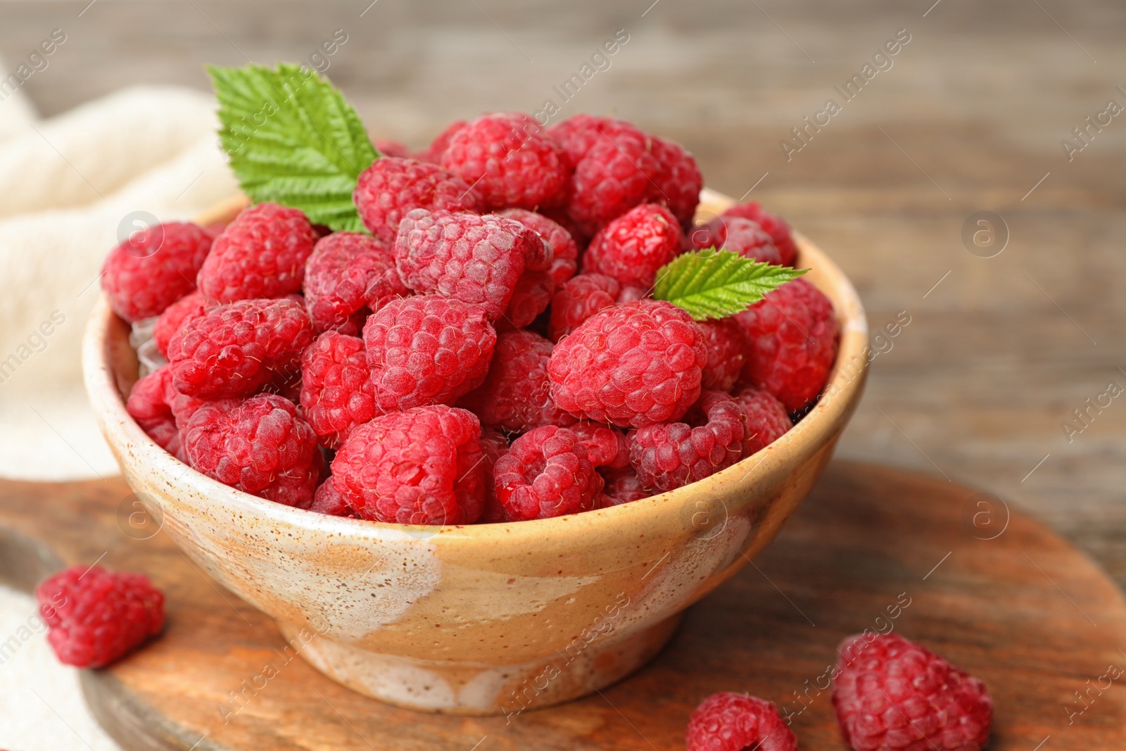 Photo of Bowl with delicious ripe raspberries on cutting board, closeup