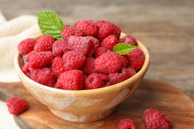 Bowl with delicious ripe raspberries on cutting board, closeup