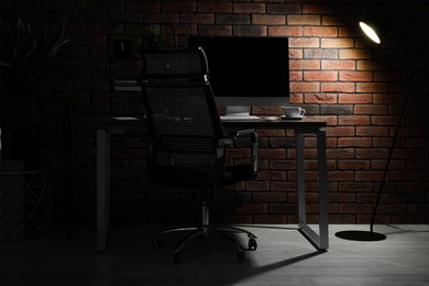 Photo of Lamp shining on cosy workplace near brick wall indoors