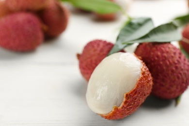 Fresh ripe lychees with leaves on white wooden table, closeup. Space for text