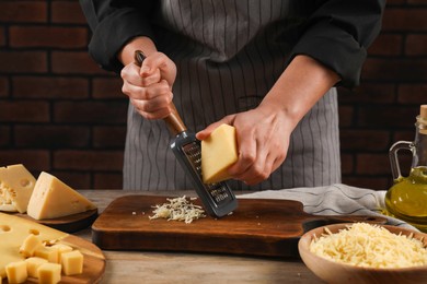 Woman grating cheese at wooden table, closeup