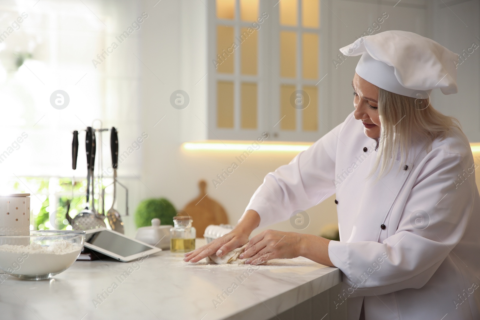 Photo of Chef with tablet cooking dough at table in kitchen